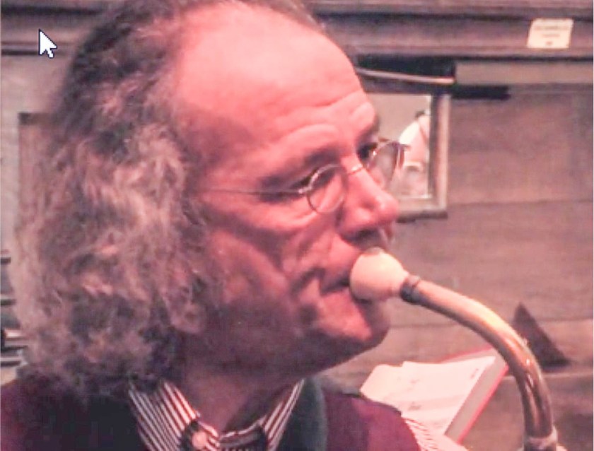 Man blowing into an old instrument called a serpent.