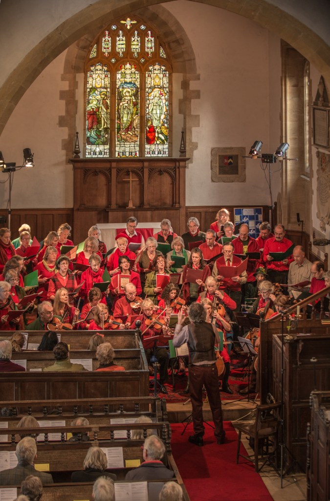 Group performing in front of an altar with a stained glass window above.
