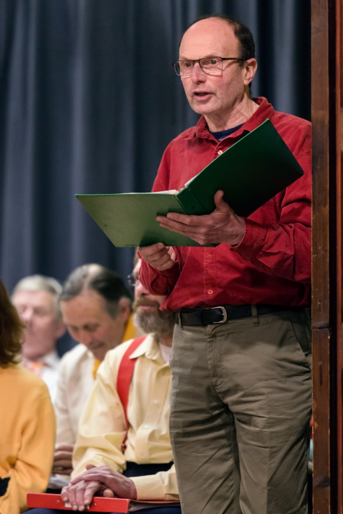 Man standing and reading aloud from a folder