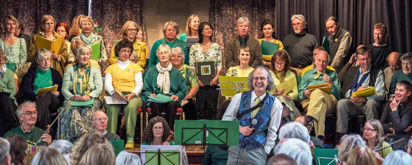 Group of singers on a stage with conductor in front making and announcement
