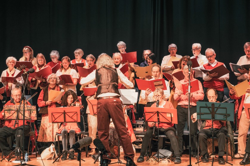 Singers and band in action with conductor with his back to the camera