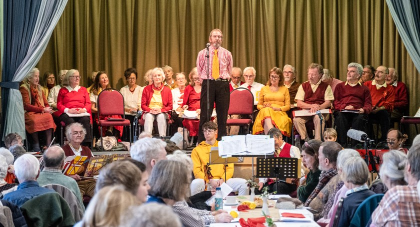 Man standing at a microphone in front of a group of seated men and women