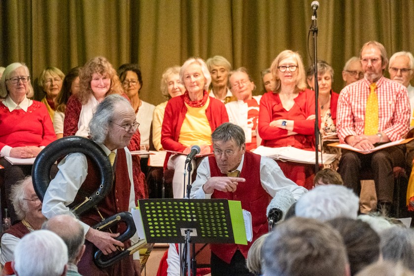 Two men making gestures in front of seated people